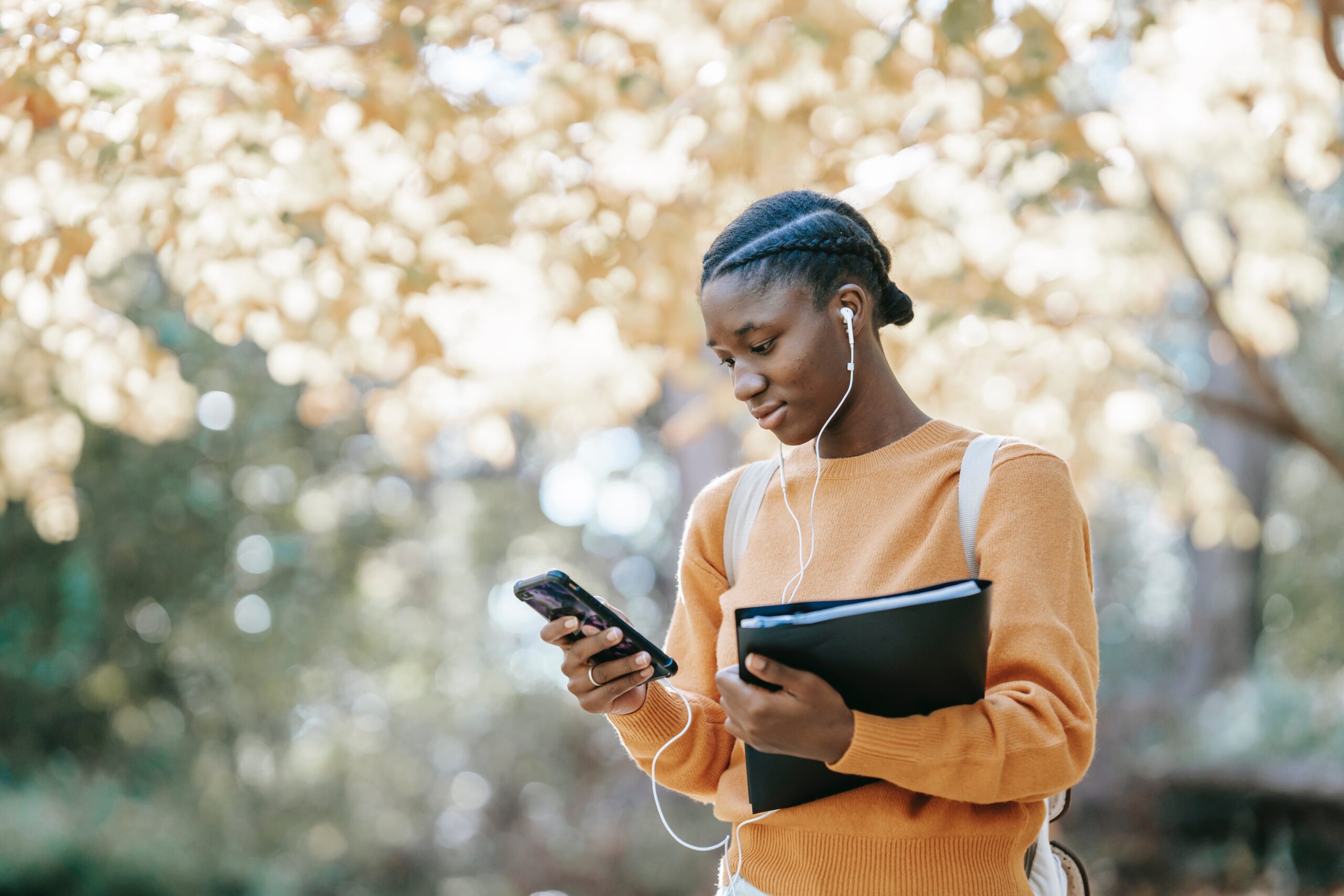 Black student listening to music using smartphone in park